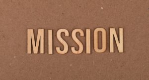 Wooden letters spelling 'MISSION' on textured cardboard background, emphasizing goals and purpose.